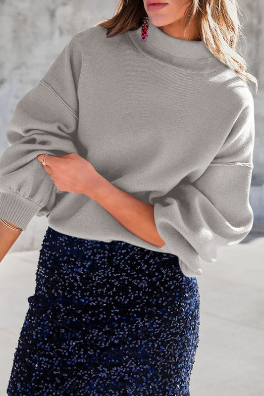 Mock neck dropped shoulder sweater in gray with slightly stretchy fabric, paired with a sequined skirt.